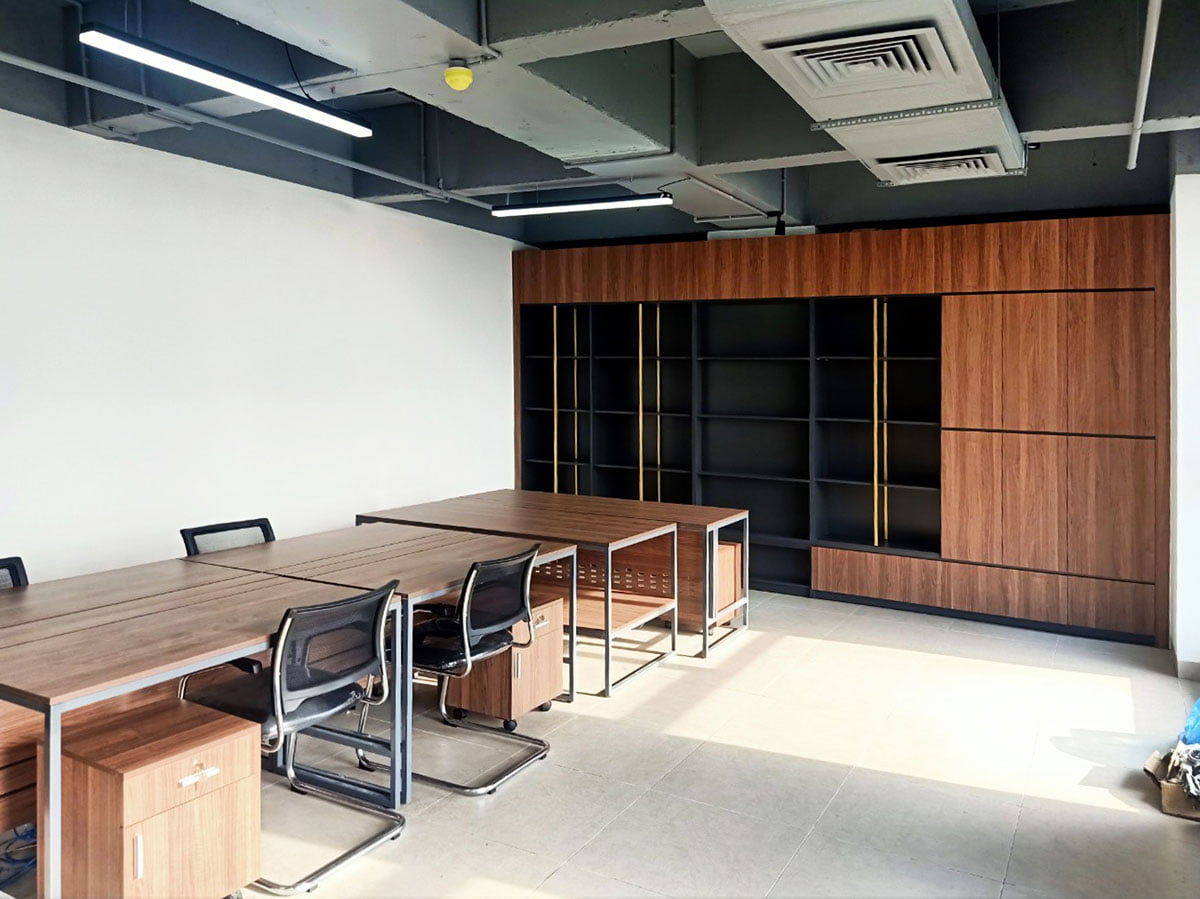 Văn phòng có bàn làm việc mặt gỗ phía trước và tủ hồ sơ gỗ chạy dọc tường phía sau